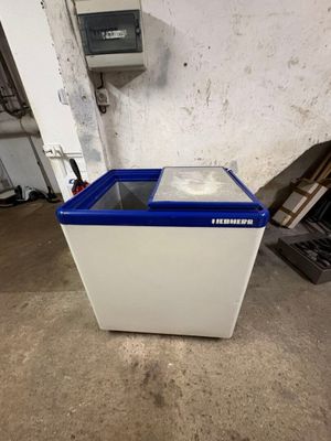 a white and blue freezer sitting on top of a floor next to a wall