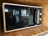 quelqu'un en train de prendre une photo d'un micro-ondes posé sur une étagère dans une cuisine