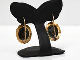 black and gold earrings on a black stand on a white surface