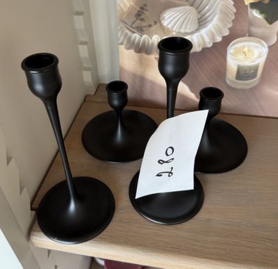trois bougeoirs noirs posés sur une table, sur laquelle se trouve un mot