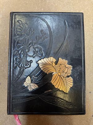 un vieux livre noir orné d'une fleur dorée sur la couverture