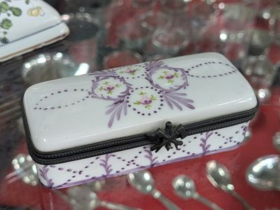 une boîte blanche ornée de fleurs violettes, posée sur une table en verre