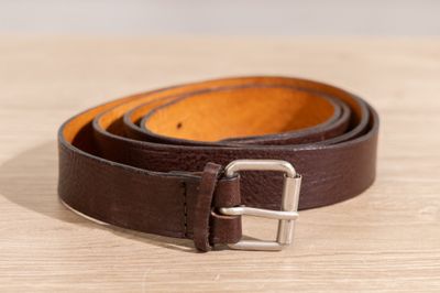 un gros plan d'une ceinture en cuir marron posée sur une surface en bois