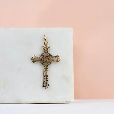 une croix en or posée sur un bloc de marbre, sur fond rose