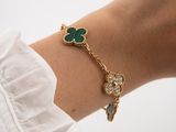 a close up of a woman ' s arm wearing a gold bracelet with green and white stones