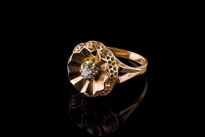 un gros plan d'une bague en or sertie d'un diamant, posée sur une surface noire