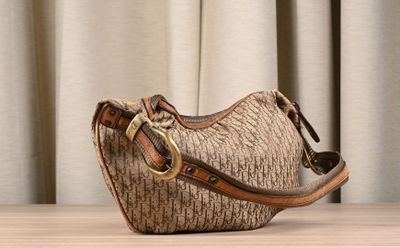 beige and brown handbag sitting on top of a wooden table next to a curtain