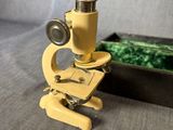 Un vieux microscope est posé sur une table, à côté d'une boîte.