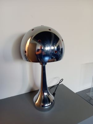 une lampe argentée brillante posée sur une table noire à côté d'un miroir