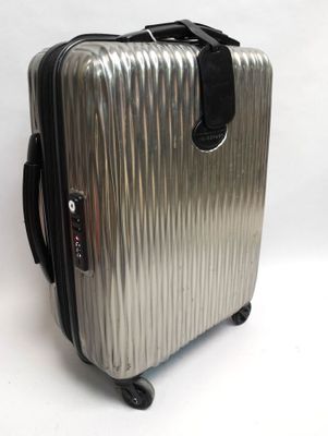 une valise argentée munie d'une poignée noire, posée sur une surface blanche