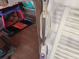un balai-vapeur violet et blanc posé sur un sol carrelé, à côté d'un radiateur blanc