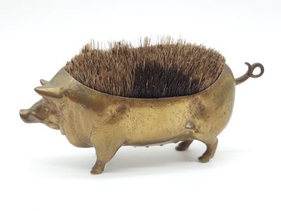 un porte-brosse en laiton en forme de cochon posé sur une surface blanche