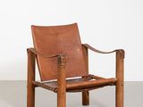 a brown leather chair with a wooden frame and arm rests against a white wall