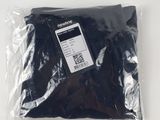 le dos d'un t-shirt noir dans un sac en plastique posé sur une surface blanche