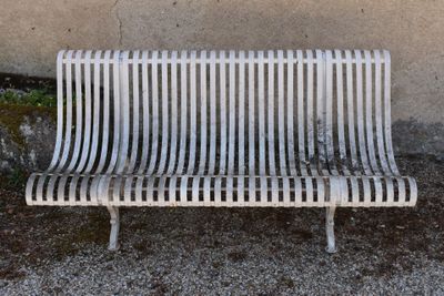 a white metal bench sitting in front of a wall