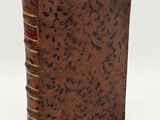 an old book with a brown cover sitting on top of a white surface