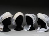 trois têtes de mannequins noires coiffées de bonnets blancs, posées sur une table