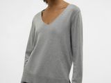 a woman wearing a grey sweater and black pants stands in front of a white background