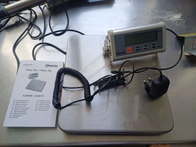 une balance numérique posée sur une table, avec un chargeur et des écouteurs