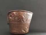 an antique copper pot with grapes and leaves on it