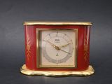 an image of a small red and gold clock on a black surface