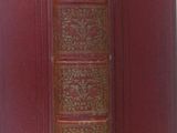 an old book with a red cover sitting on top of a white surface