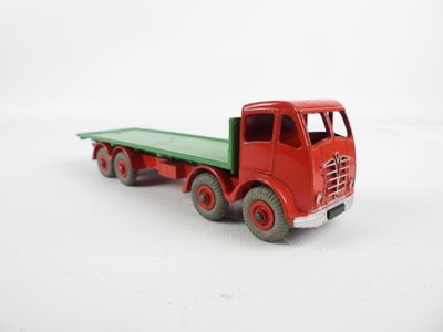 un camion jouet rouge avec une benne verte posé sur une surface blanche