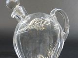 bouteille en verre transparent avec une anse, posée sur un support noir