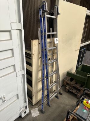 une échelle appuyée contre un mur, à côté d'une pile de palettes