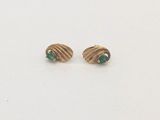 une paire de boucles d'oreilles en or et émeraude posées sur un fond blanc