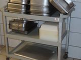 Plusieurs casseroles et poêles sont empilées sur un chariot métallique dans une cuisine.