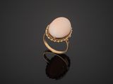 a gold ring with a white stone on a black surface