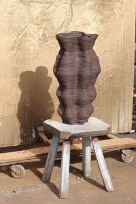 un grand vase marron posé sur un tabouret devant un mur