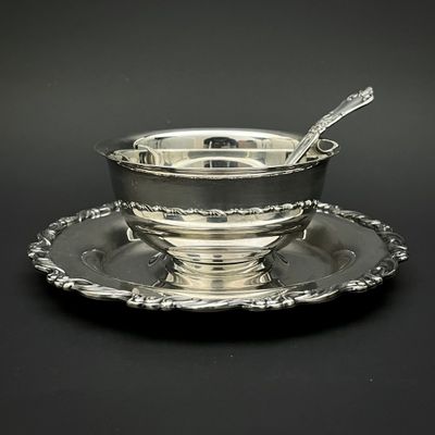 un service en argent ancien composé d'un bol et d'une cuillère posés sur une soucoupe
