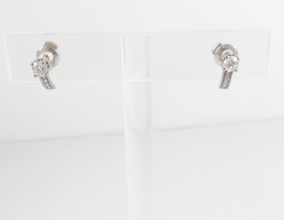 une paire de boucles d'oreilles en argent posée sur un socle en acrylique transparent, sur un fond blanc