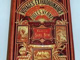 an old book on a white surface with a red cover and gold lettering