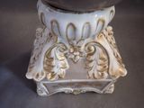 a white and gold vase on a stand on a table