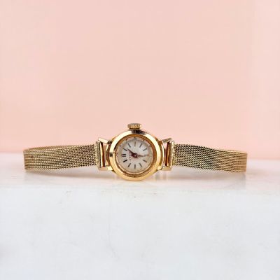 gros plan d'une montre-bracelet en or sur une surface blanche