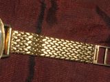 une montre-bracelet en or avec un cadran blanc posée sur un tissu rouge