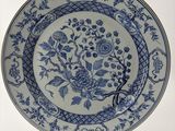 assiette bleue et blanche ornée de fleurs et d'oiseaux, posée sur un socle