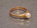 une bague en or sertie d'une perle, posée sur une table