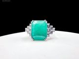 an emerald and diamond ring on a white surface