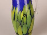 a blue and green vase with a bunch of green bananas on it