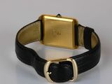 an image of a gold watch with a black leather band on a white surface