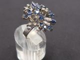 a close up of a diamond and sapphire cluster ring on a clear acrylic base