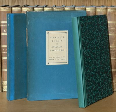 Plusieurs livres sont empilés sur une étagère, devant une autre étagère remplie de livres.