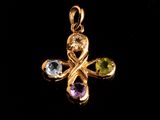 un pendentif en forme de croix en or, orné de pierres multicolores sur fond noir