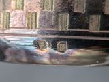a close up of a silver vase with buildings in the background