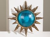 un soleil en laiton avec un verre bleu au centre, posé sur une étagère blanche