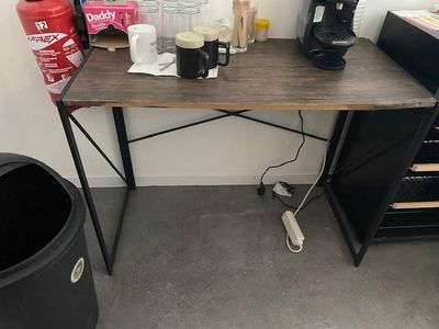 a desk with a coffee maker and a trash can on it